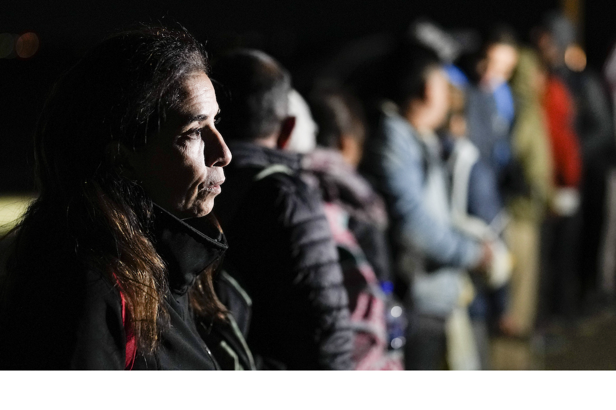 Woman at the border, with line of migrants out of focus behind her. Jan 2023