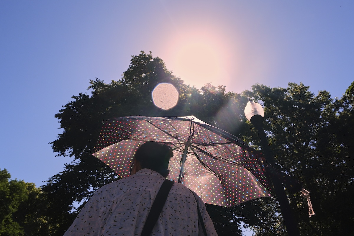 Person blocks high overhead sun with umbrella Boston 06-24-2025